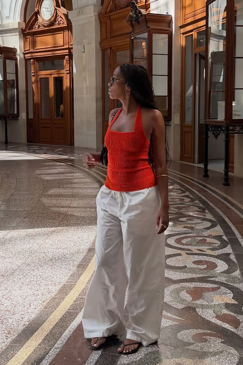 a woman wearing a red halter tank top, white pants, and black flip flops