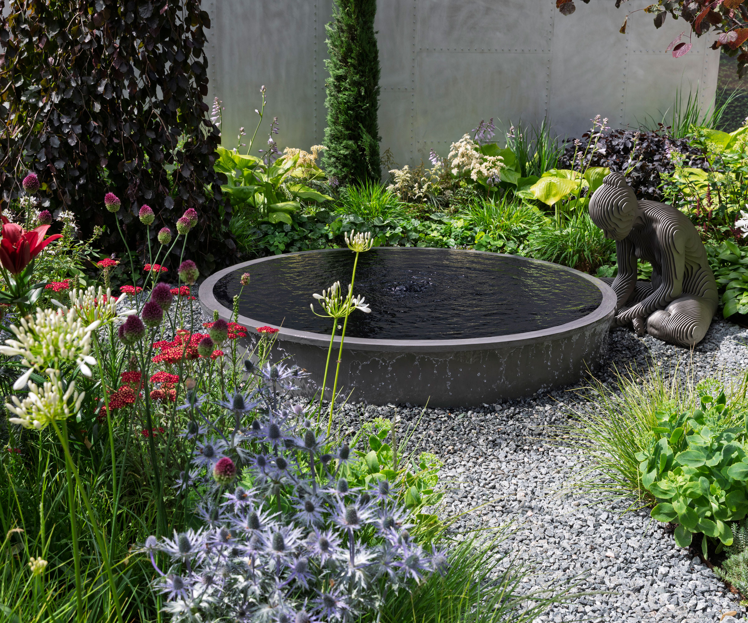 modern garden pond with garden sculpture, gravel landscaping and colourful planting