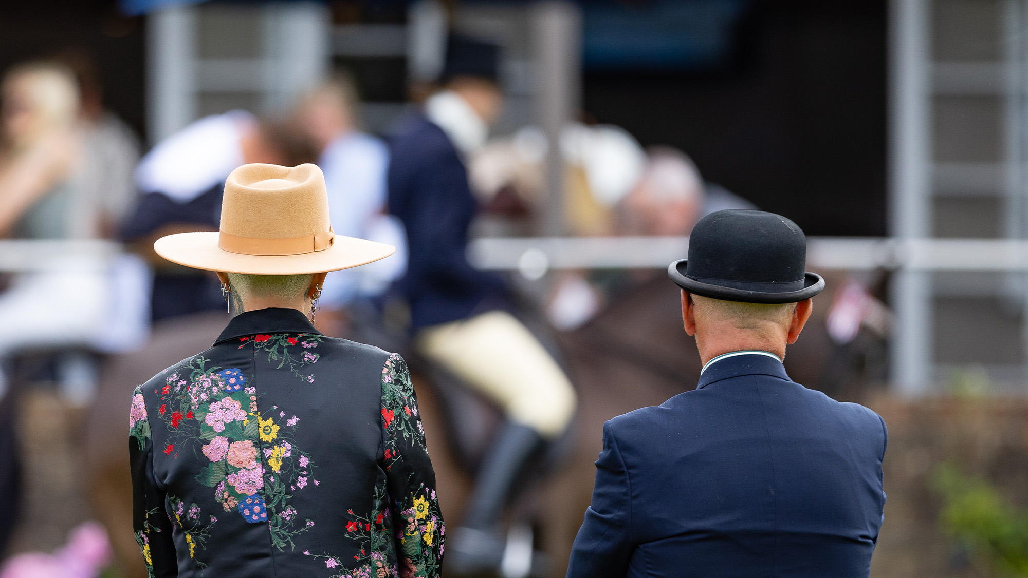 Two judges viewed from rear watching an unidentifiable horse and rider in the background