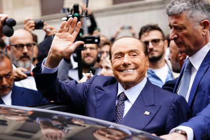 A picture of Silvio Berlusconi waving and smiling while surrounded by people