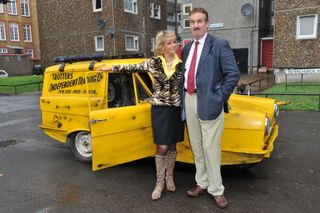 John Challis as Boycie with his on screen wife in front of a yellow three wheel car