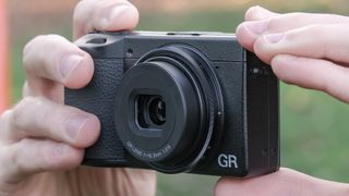 Ricoh GR IV compact camera held in a pair of hands