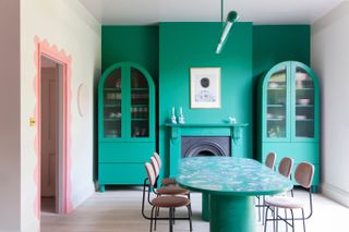 A dining room with deep green cupboards