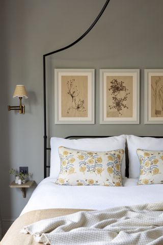 gray bedroom with black iron bed, artwork, floral cushions, oatmeal throw, tiny wall mounted bedside, wall light