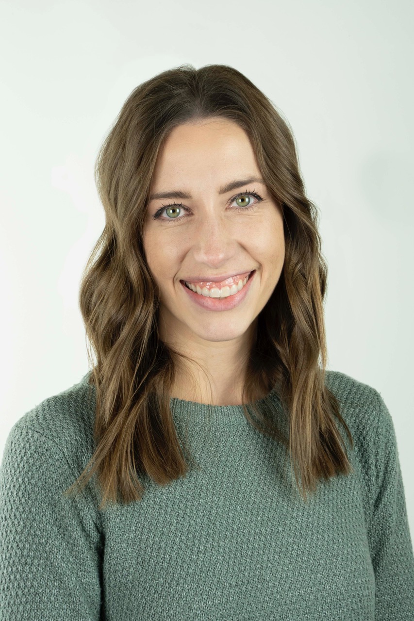 Woman with long brown hair wearing a khaki green sweater and smiling