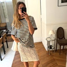 Influencer Anne Laure Mais wears a sheer lace skirt and an oversized striped crewneck top. She sports a white leather shoulder bag and MiuMiu ballet flats. 