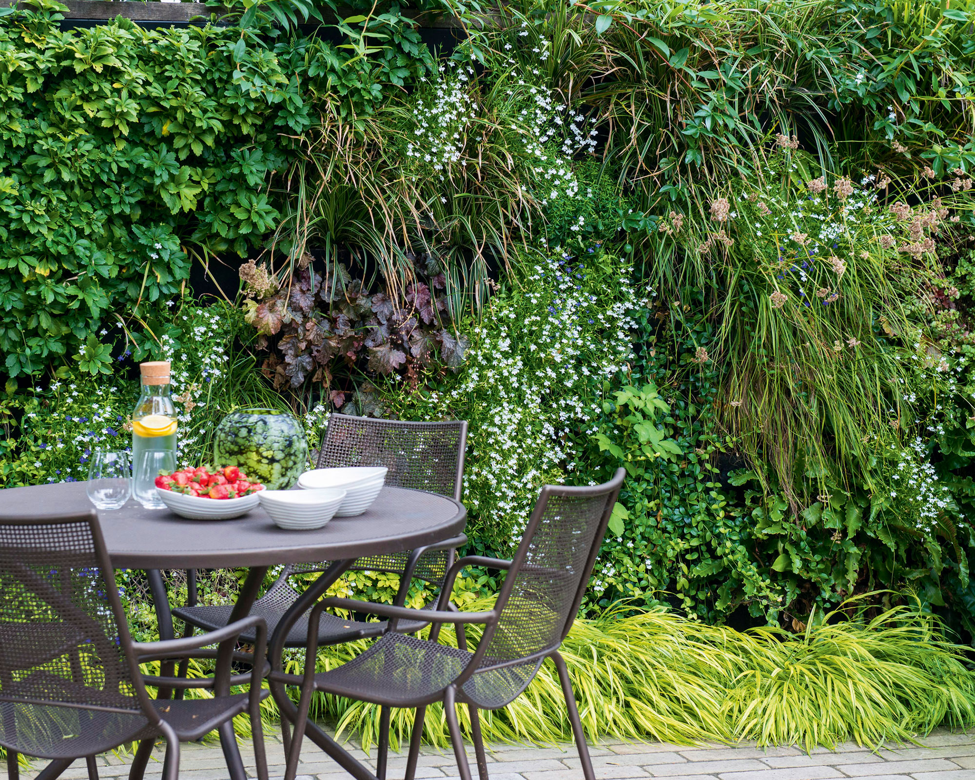 A black outdoor dining table and chairs in front of a vast living wall