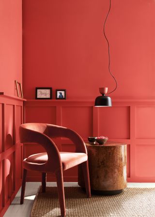 A modern living room with wood panelling painted in a pinky red with a modern chair and a pendant light