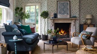 modern country living room with open fire blue velvet sofa and woodland print wallpaper demonstrating key interior design trends 2022