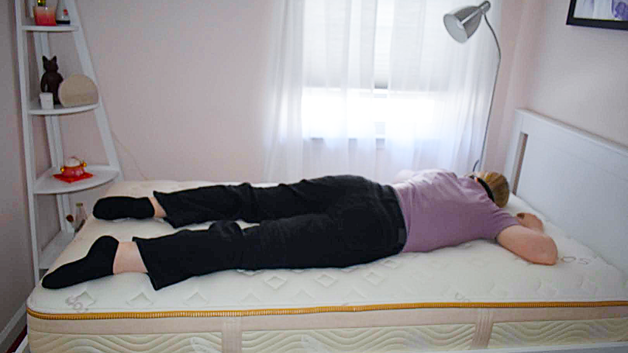 Tester with an eye mask sleeps on her stomach on a bare Saatva Memory Foam Hybrid Mattress