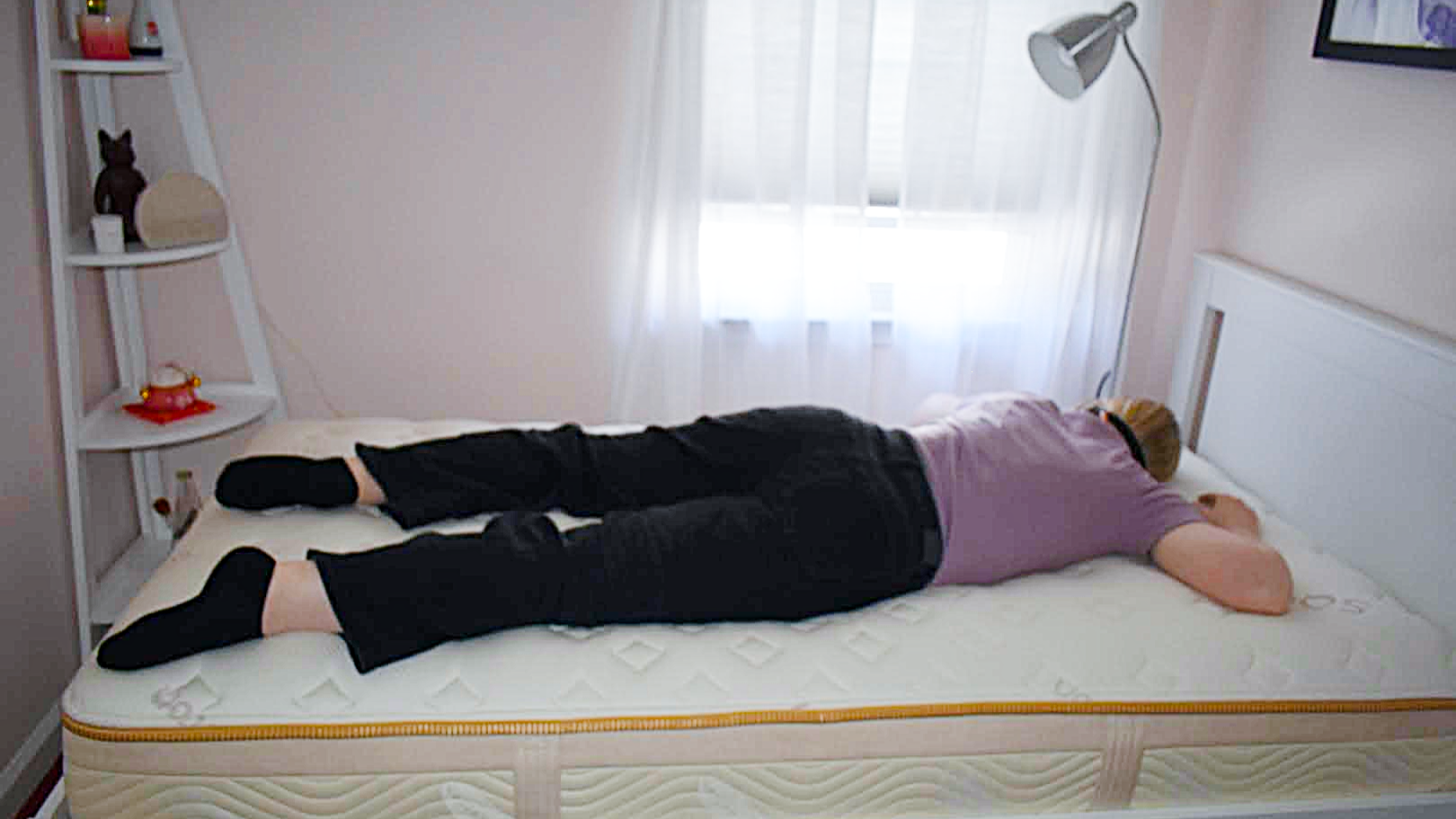 Tester with an eye mask sleeps on her stomach on a bare Saatva Memory Foam Hybrid Mattress
