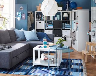 A blue living room with white open shelving used as room divider and white coffee table with caster wheels