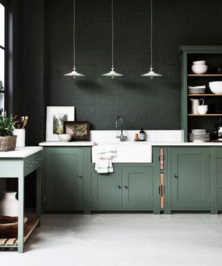 Dark green kitchen with a white Belfast sink below three pendant lights
