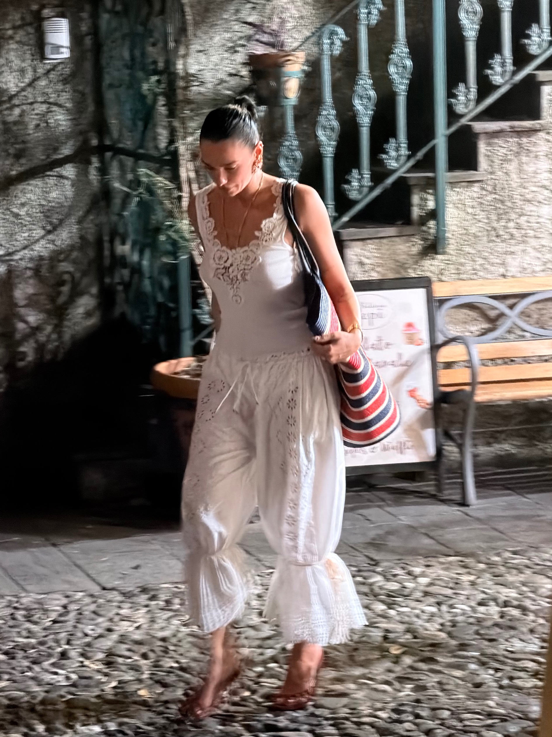 Dua Lipa walks down the street wearing bloomer trousers with a white lace-trim tank top.