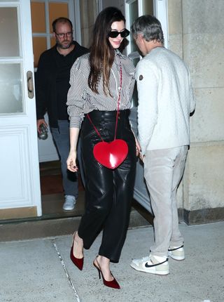 anne hathaway wears a striped button-up with leather pants and a red heart bag