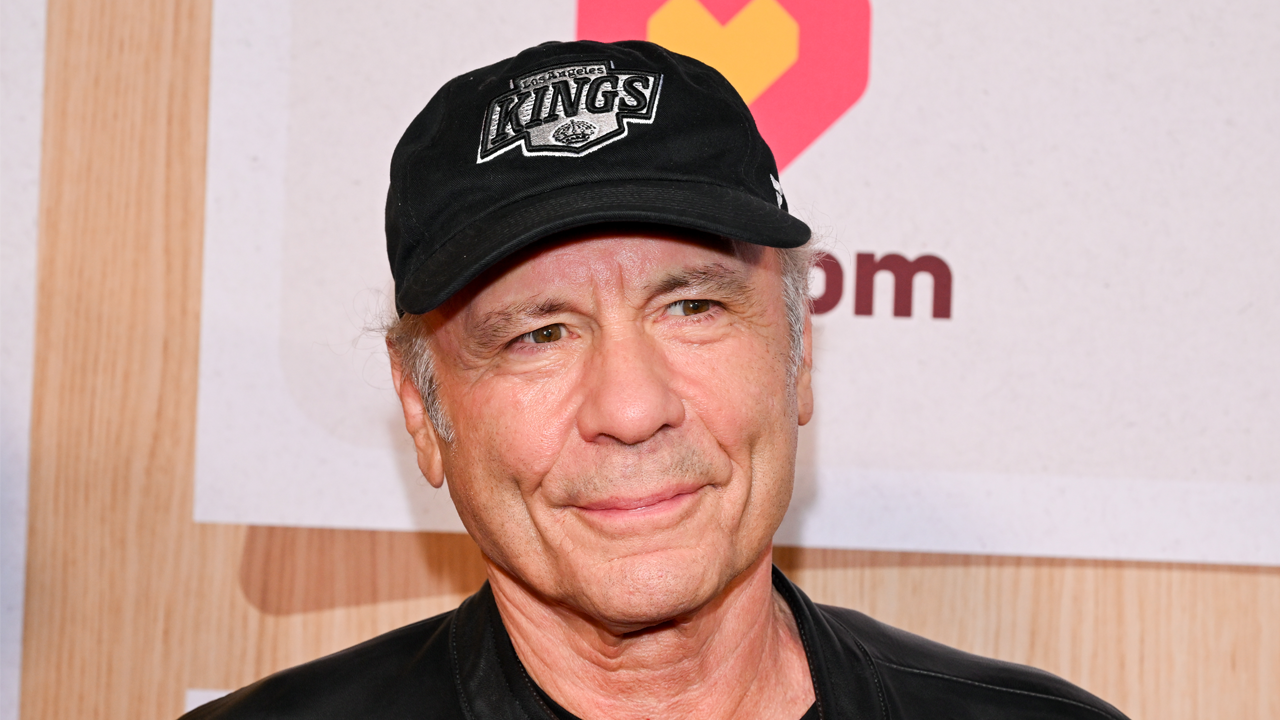 Bruce Dickinson smiling in a black baseball cap