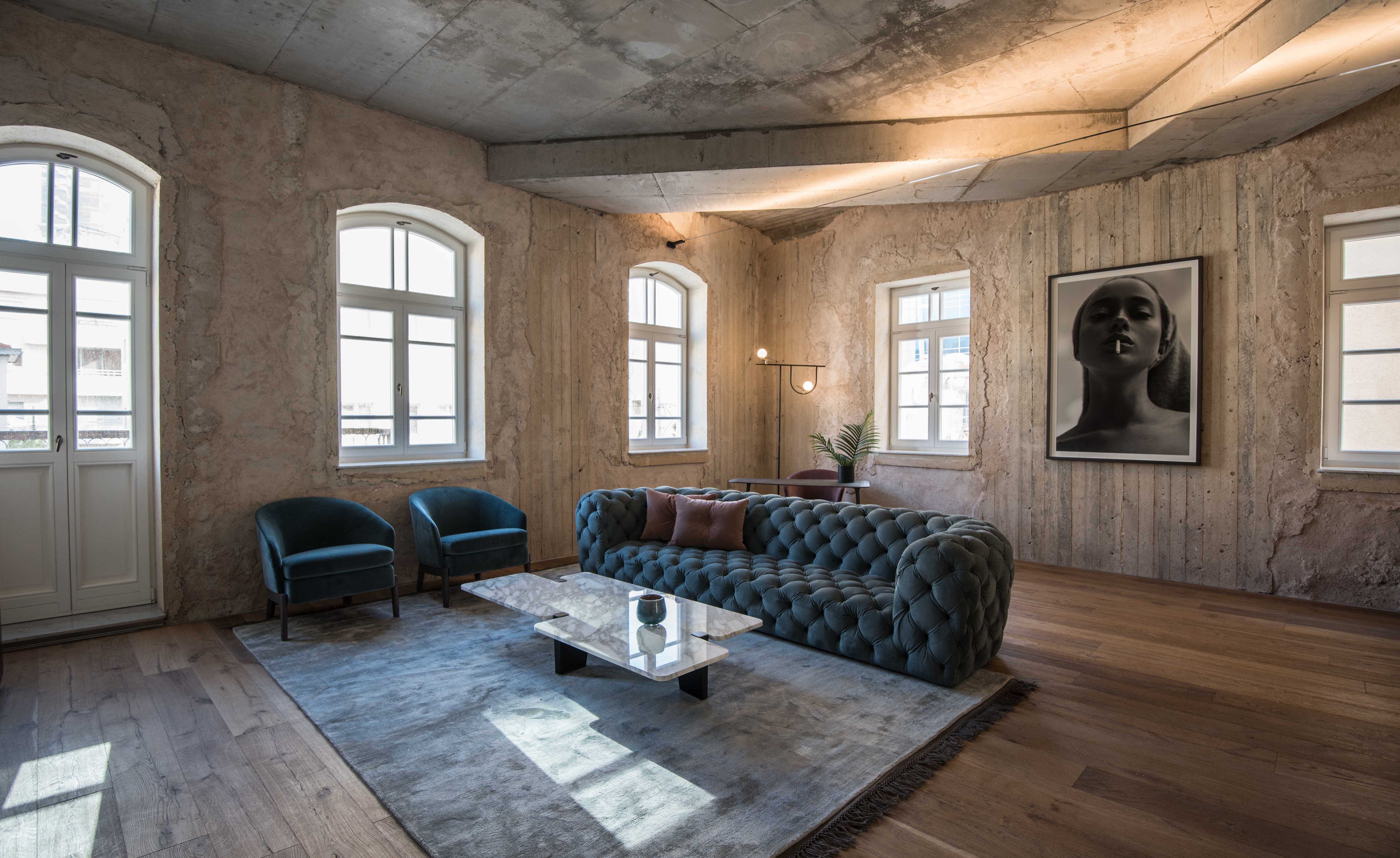 Large couch with 2 single couches around coffee table, finished wooden floors with exposed concrete