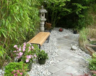 slate slab pathway in ornamental, domestic garden featuring Japanese elements, modern wooden bench, potted azaleas, granite lanterns, bamboo hedging, koi fish pond and Japanese maples (acers)