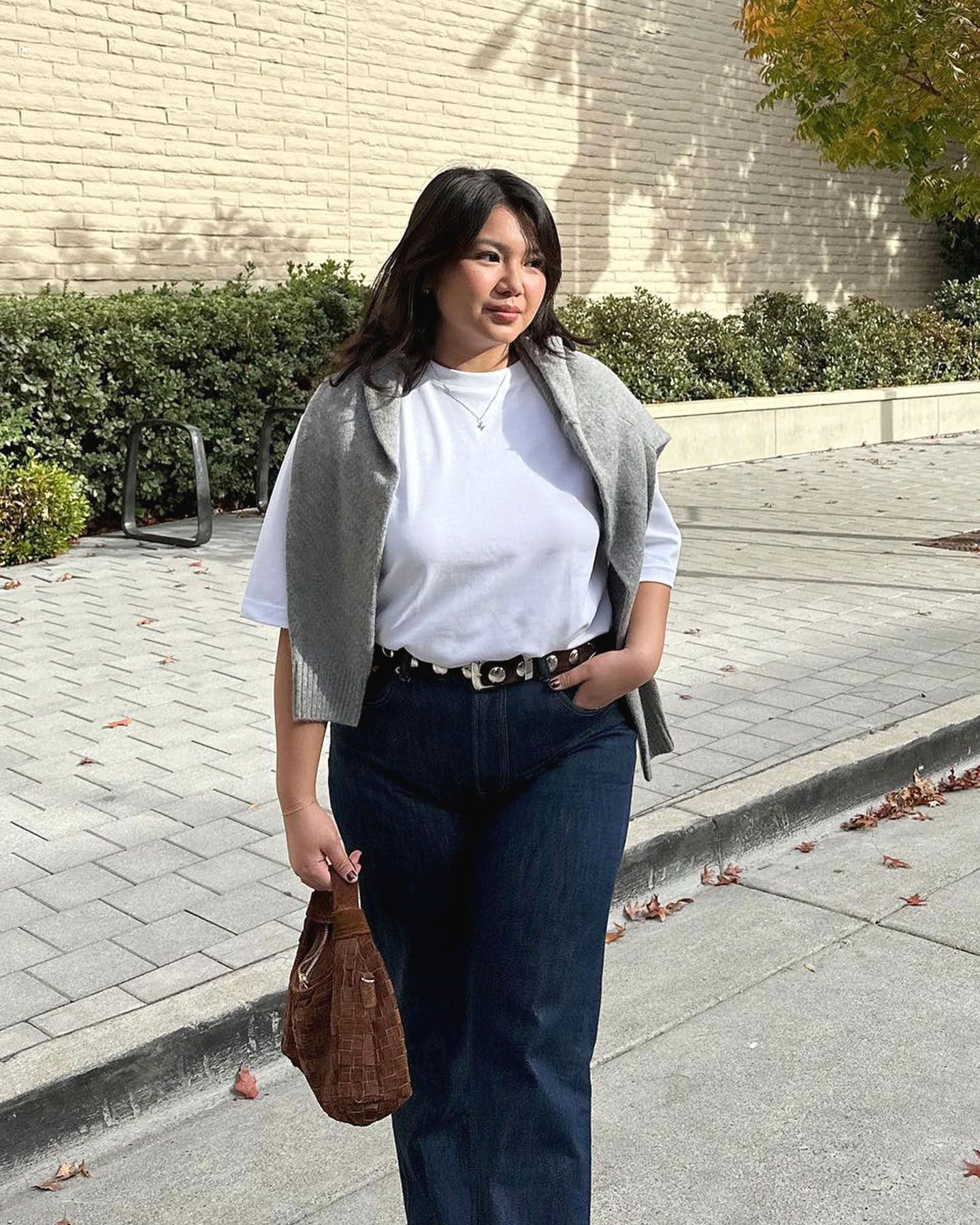 Marina Torres wearing a white tee, dark-wash jeans, and a gray sweater draped over her shoulders.
