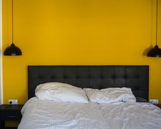 Yellow bedroom walls with black overhead lights and black headboard with white sheets