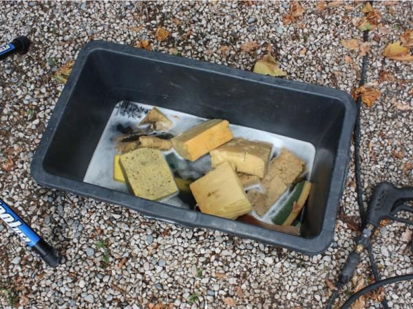 Tools of the trade: a tub full of soapy sponges and brushes, a pressure washer, and the legs of a Euro-style repair stand.