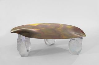 A table with a leaf-like tabletop, in brown color with other translucent colors. The table has see-through legs.
