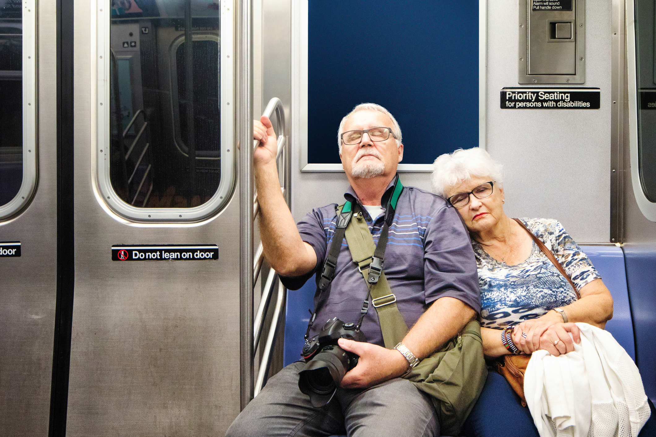 Exhausted senior tourist couple sitting in subway train after a long day out. The female is resting her head on her companion's arm.