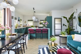 Open-plan kitchen-diner with teal kitchen, pink bar stools, dark wood dining set and monochrome geometric striped rug