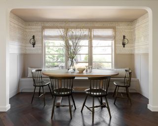 neutral dining area with oval wooden table, dark Windsor chairs and patterned wallpaper