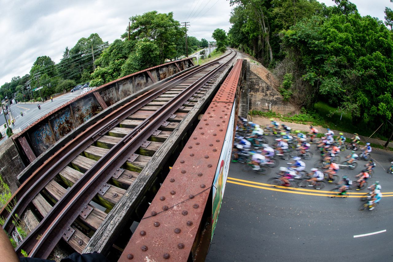 The women's peloton passes underneath a railroad bridge.