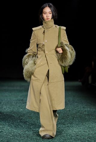 a photo of the fall jacket trend, funnel neck coats shown in Burberry's runway show with a model wearing an olive green trench coat with matching trousers and green boots