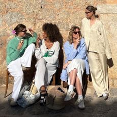 a group of European fashion friends including Amaka Hamelijnck sit on a bench wearing stylish Scandi-inspired outfits with oversize button-downs, linen pants, and sneakers while chatting and eating ice cream