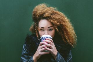 Portrait of woman drinking coffee to go in front of a green wall