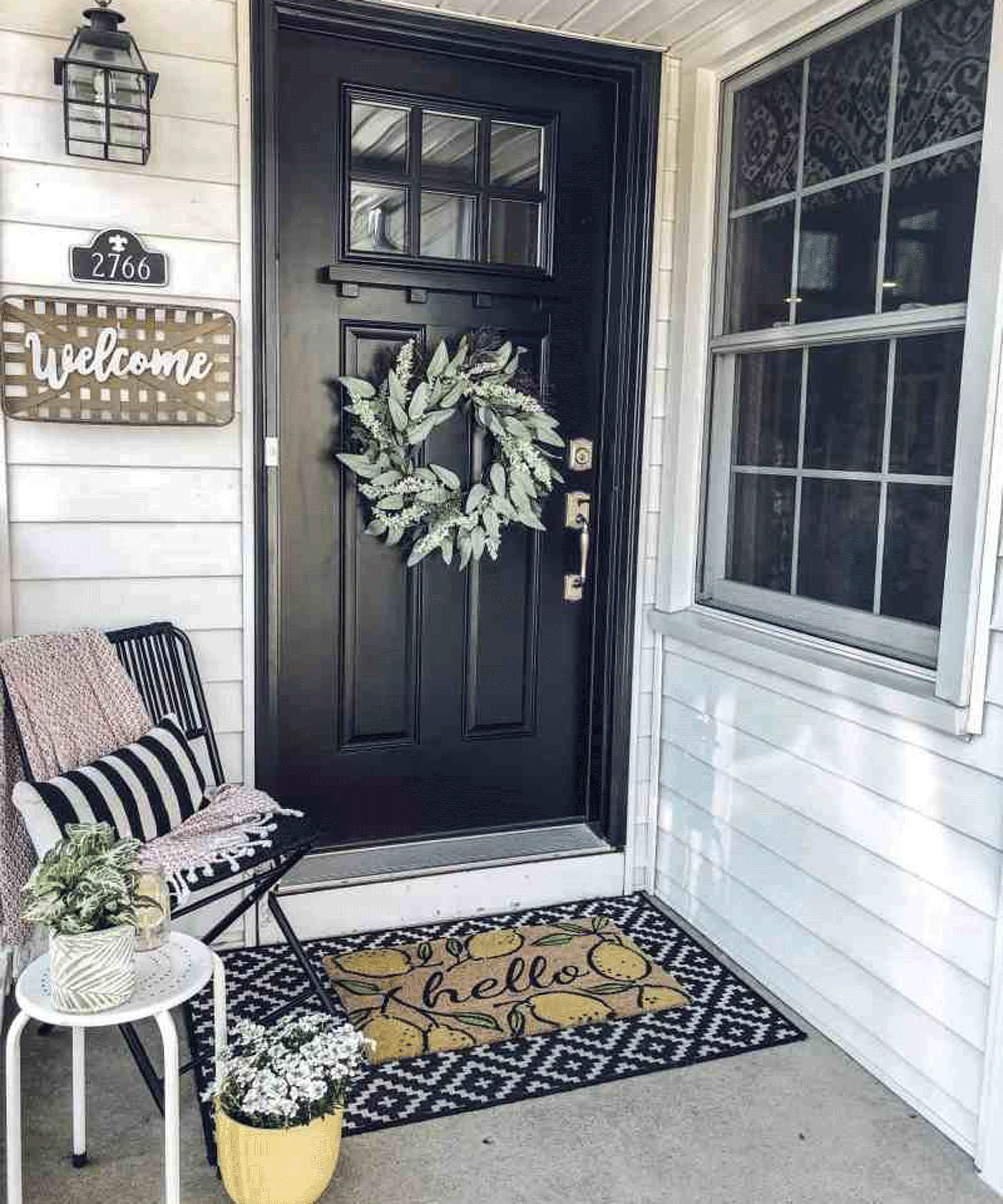 Rustic porch full of mixed textures, with wreath on door, and hello doormat, and welcome sign on wood paneling exterior.