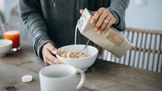 A woman pouring milk over a bowl of cereal on the kitchen counter