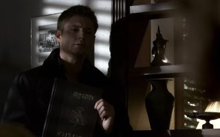 Dean holding ancient book in Supernatural