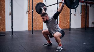 Man performs overhead squat with barbell in gym