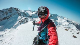 man in red coat stook on a snowy mountain top with a gopro