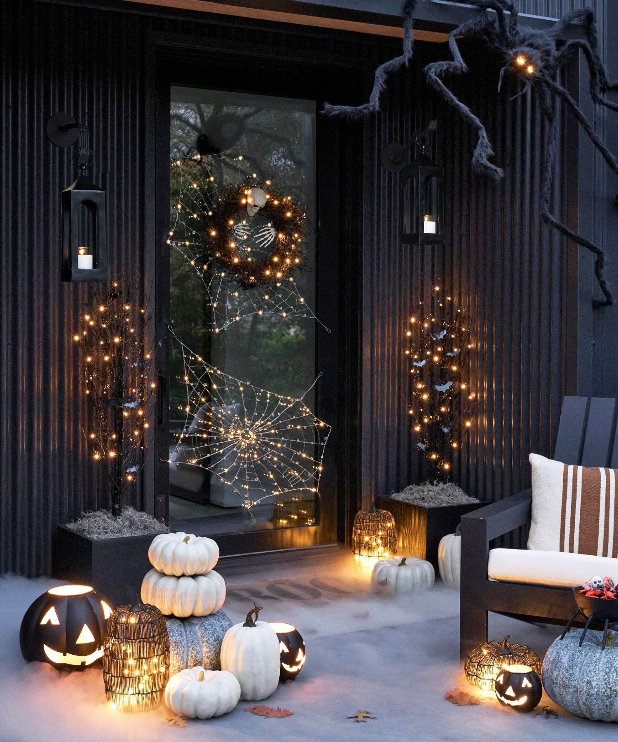 Black porch with halloween decor and lighting, large spider decoration in the corner of the door and pumpkins dotted around the porch