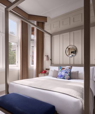 The Kimpton Bed on a fourposter against beige panelled walls and French windows. 