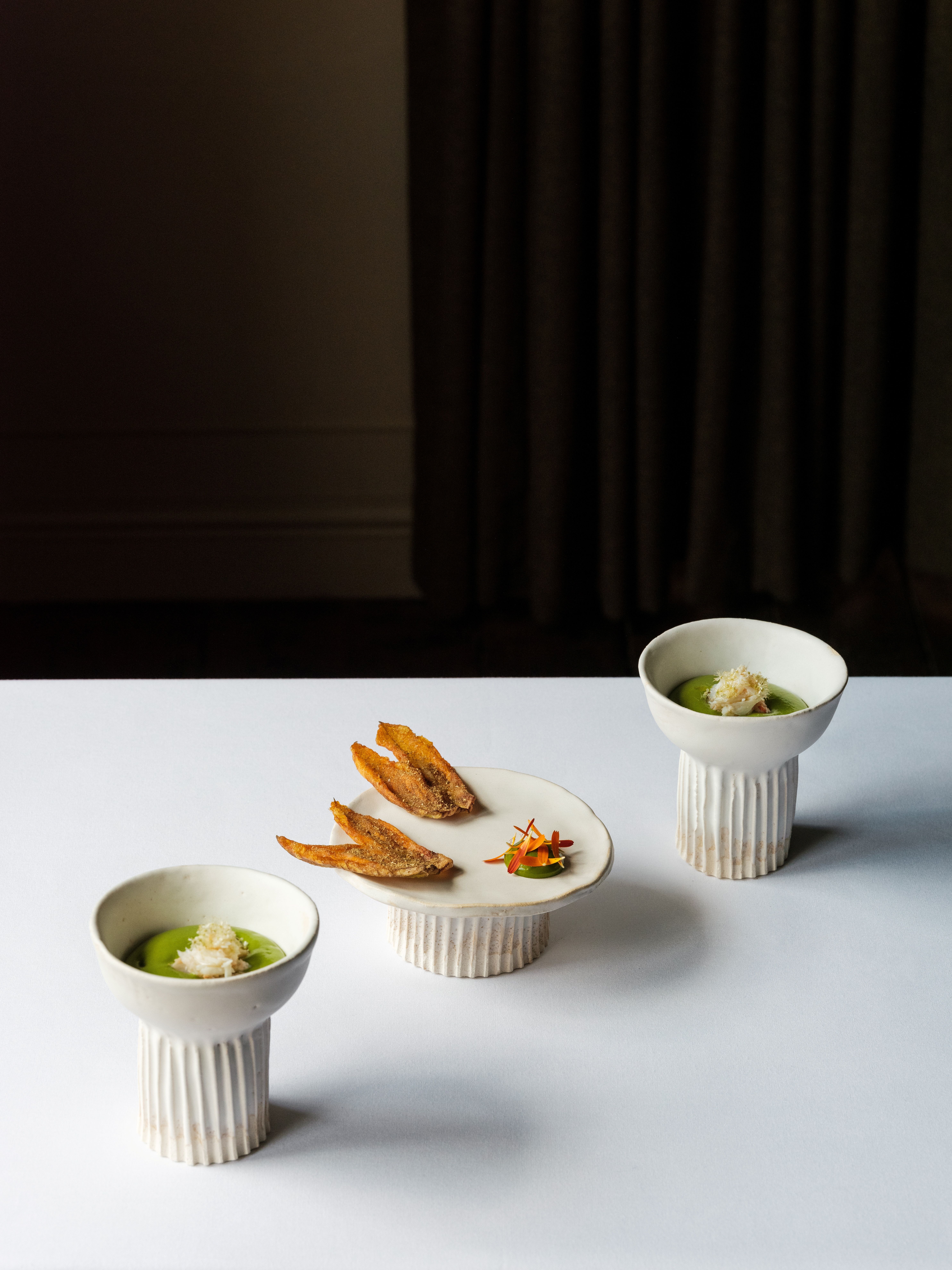 A series of shots depicting the interiors of a modernly renovated, old farmhouse in the countryside, mixing a rustic frame with plush textiles, textural surfaces, glass, wood, and chrome accents, and colorfully plated dishes.