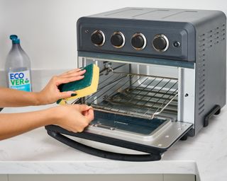 Real Homes reviewer Christina Chrysostomou cleaning Cuisinart Air Fryer Toaster Oven with sponge and Ecover dish soap