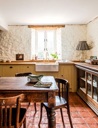 Period kitchen with tiled floor, yellow painted cabinets and rustic dining table and chairs