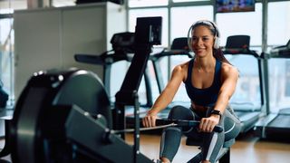 A woman exercising on a rowing machine while observing her workout stats on an adjacent monitor