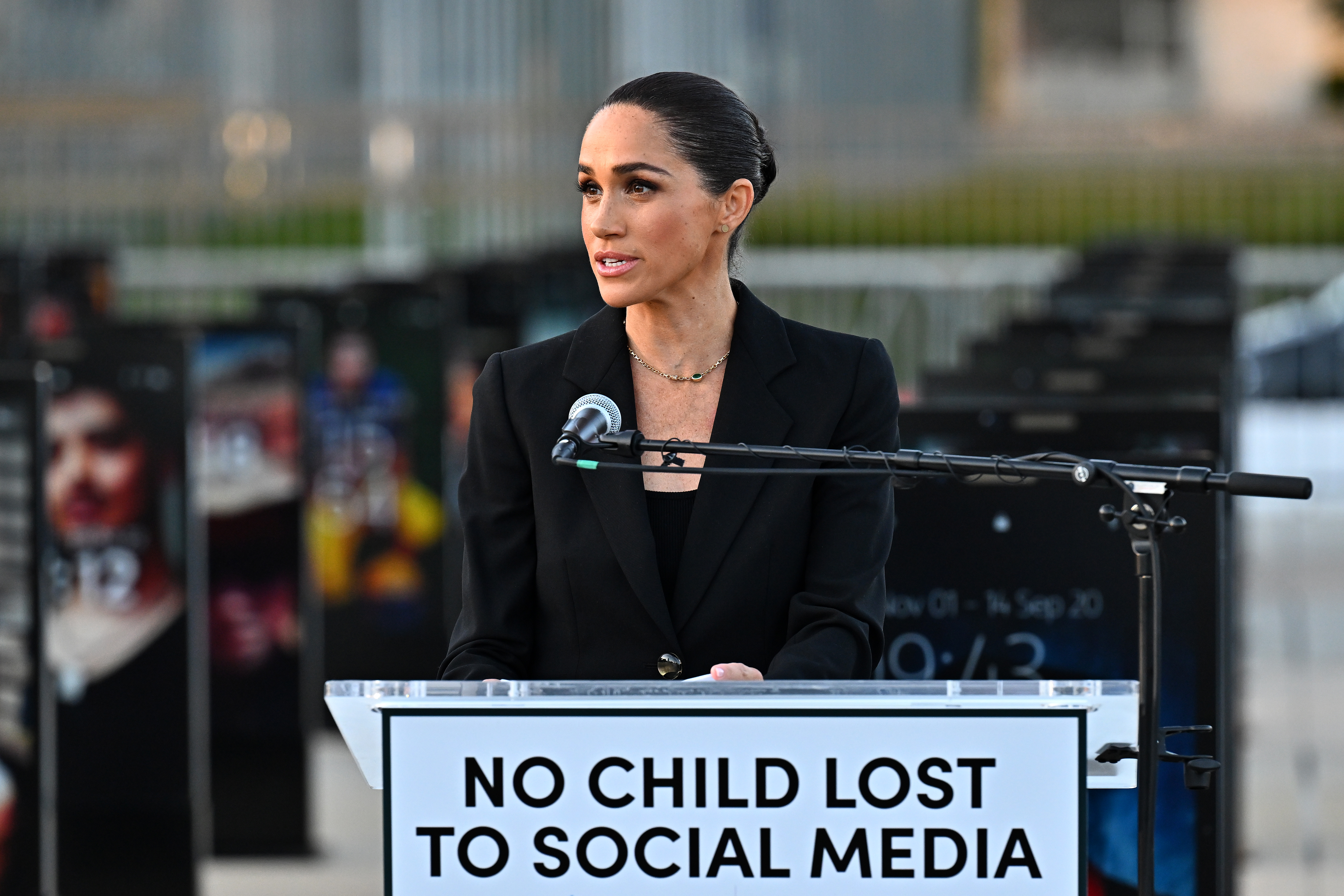 Meghan Markle wearing a black suit speaking into a microphone