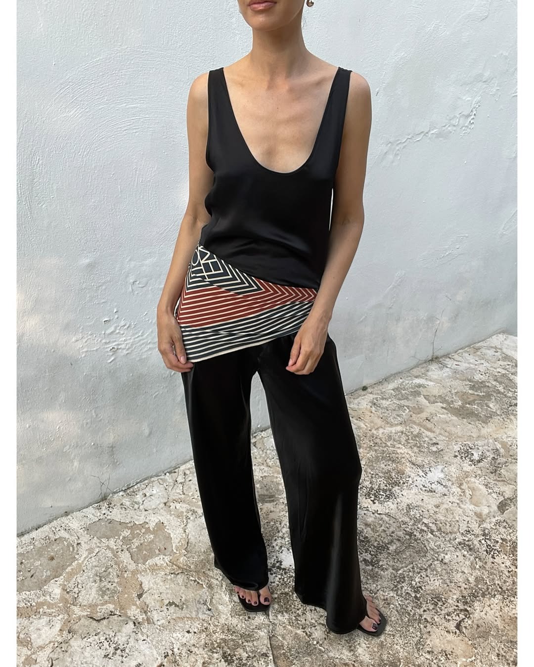 Woman in black satin pants, a silk scarf tied around her waist, and a black silk top.
