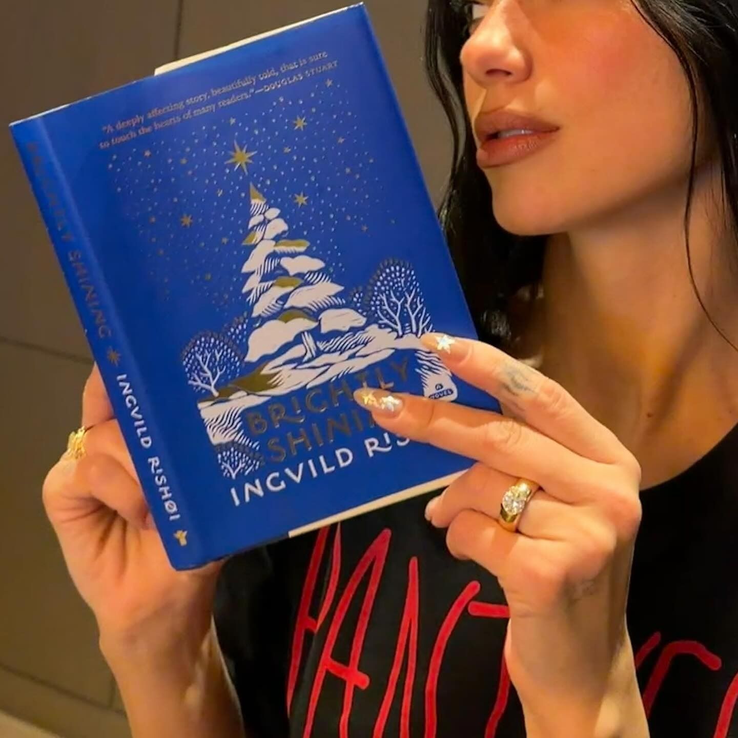 Dua Lipa holding a blue book while showing her silver and gold starry nails