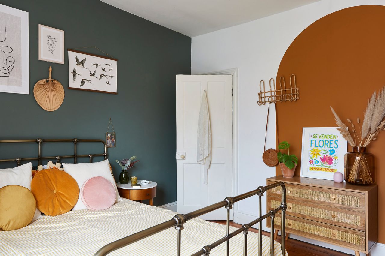 master bedroom with one dark wall and an orange painted arch with rattan furniture and a black metal bed