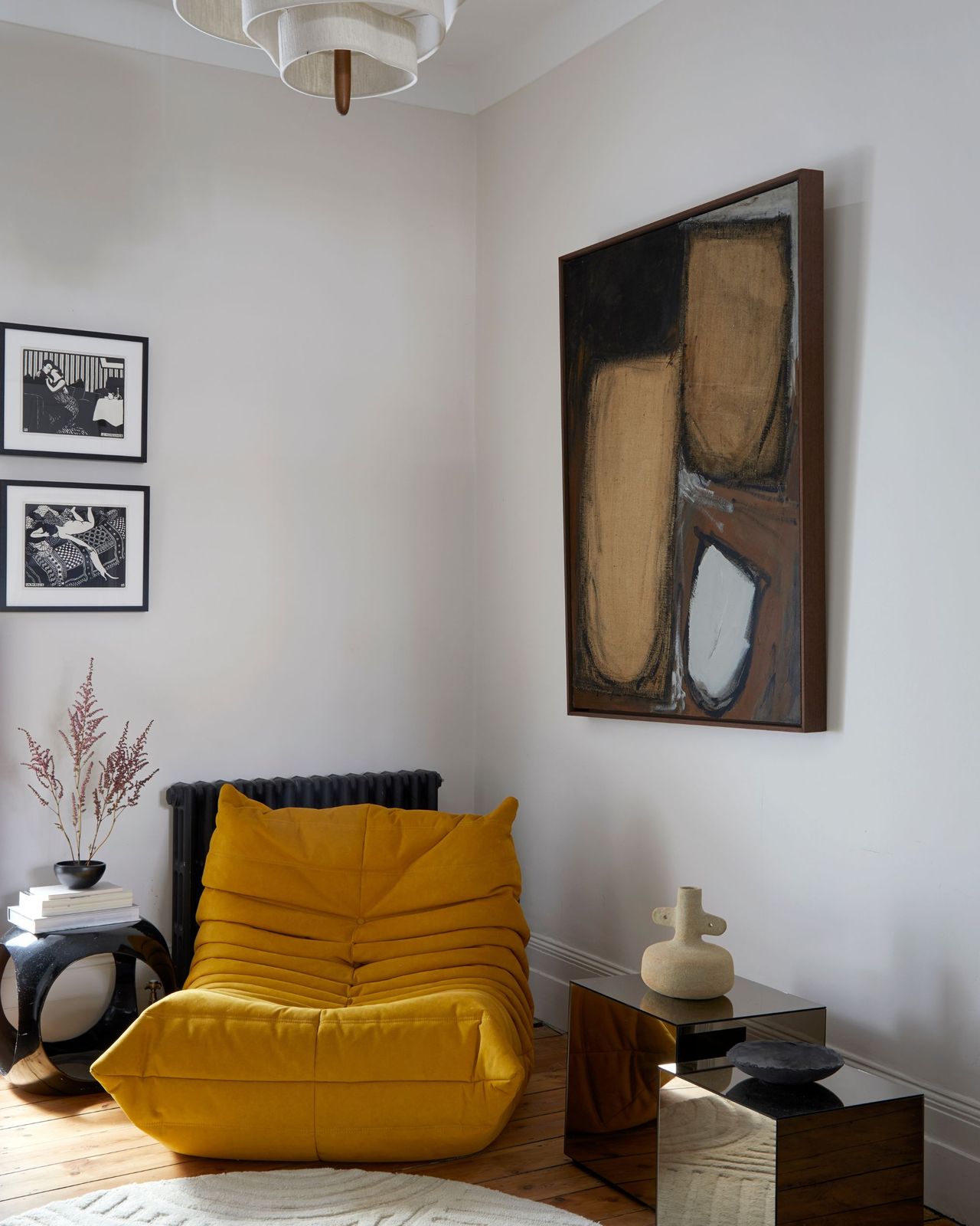 A corner seating area with a yellow togo-style accent chair surrounded by artwork and side tables
