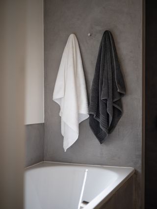 Two towels hanging on hooks against a grey wall